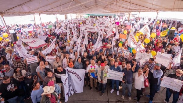 Carlos Torres Piña hablando ante una multitud numerosa en un evento al aire libre en Michoacán, con banderas y pancartas visibles