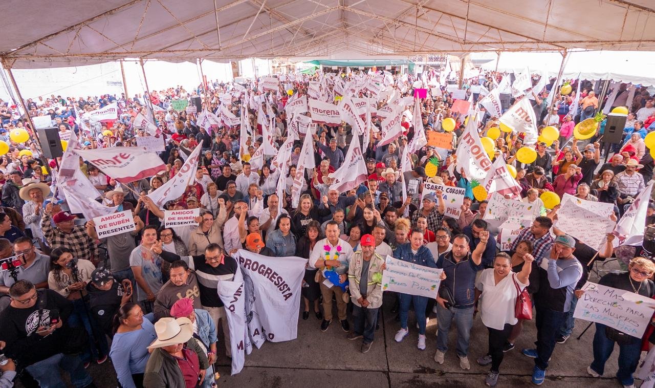 Carlos Torres Piña hablando ante una multitud numerosa en un evento al aire libre en Michoacán, con banderas y pancartas visibles