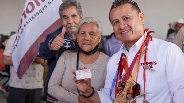 Carlos Torres Piña hablando en un evento público en Morelia, Michoacán, con fondo de bandera mexicana y letreros sobre pensiones del Bienestar