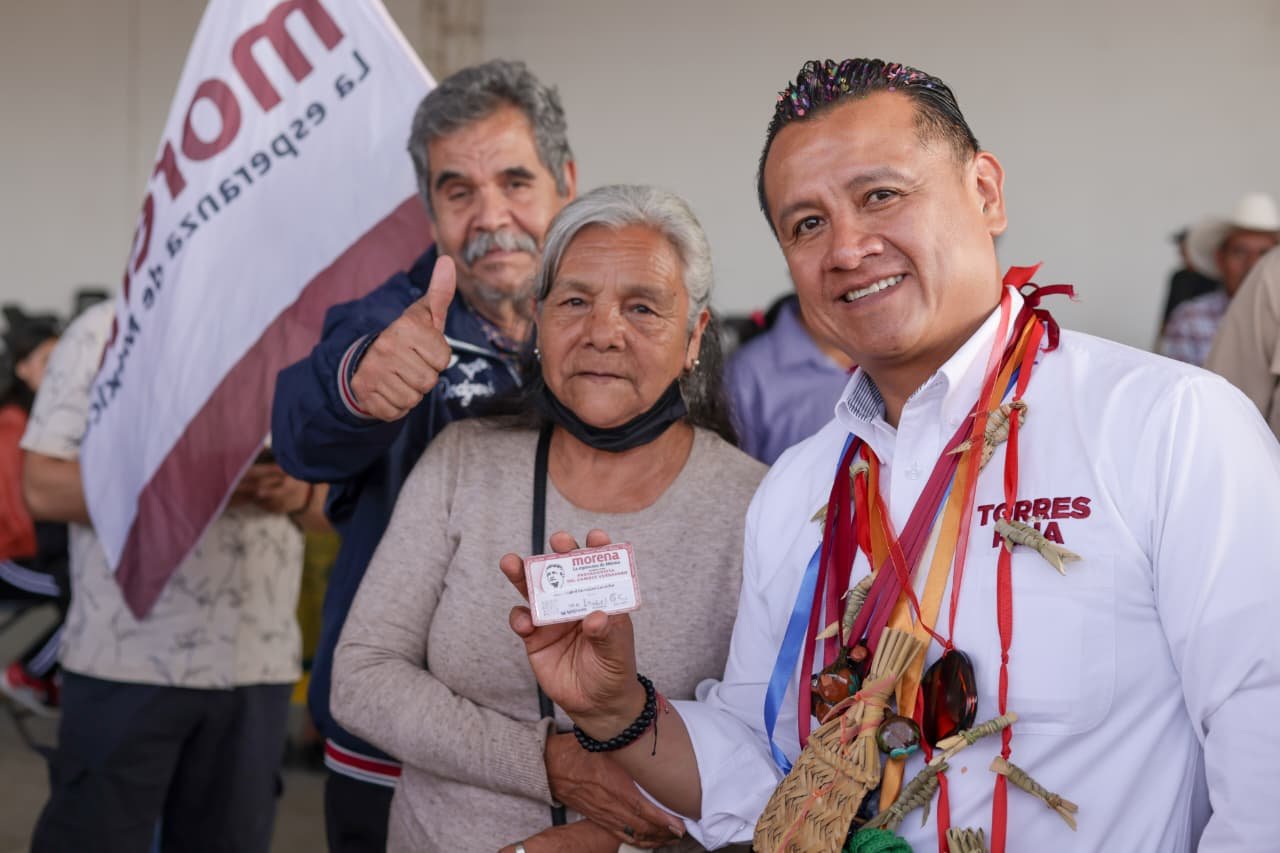 Carlos Torres Piña hablando en un evento público en Morelia, Michoacán, con fondo de bandera mexicana y letreros sobre pensiones del Bienestar