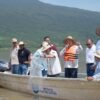 Personal de Compesca liberando crías de pez blanco en el lago de Pátzcuaro, con el paisaje lacustre al fondo
