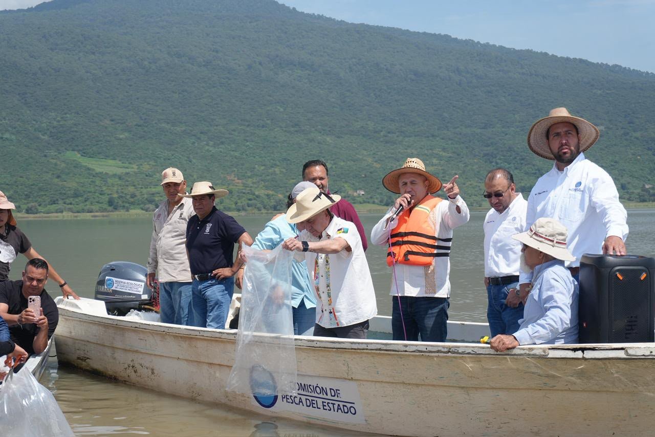 Personal de Compesca liberando crías de pez blanco en el lago de Pátzcuaro, con el paisaje lacustre al fondo