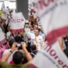 Carlos Torres Piña en campaña: hablando ante público en un municipio, con fondo de banderas y letreros de su nombre