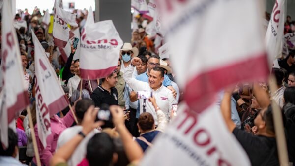 Carlos Torres Piña en campaña: hablando ante público en un municipio, con fondo de banderas y letreros de su nombre