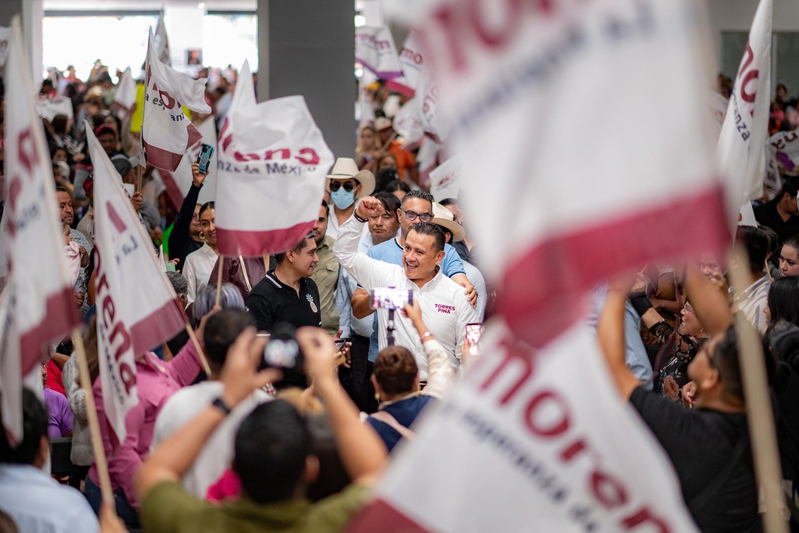 Carlos Torres Piña en campaña: hablando ante público en un municipio, con fondo de banderas y letreros de su nombre