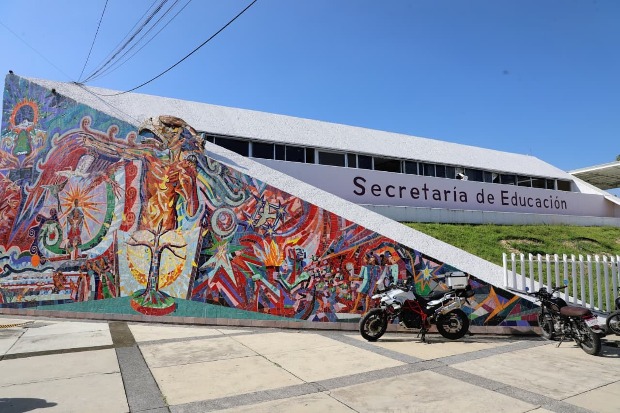 Logotipo de la Secretaría de Educación del Estado de Michoacán junto a una escuela secundaria en entorno rural de San Francisco Peribán