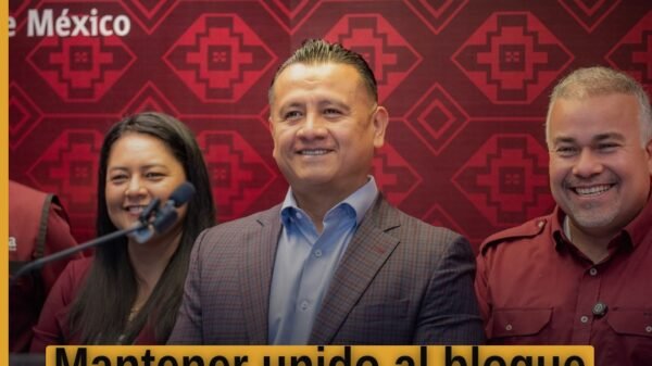 Carlos Torres Piña hablando ante micrófonos en un evento público en Michoacán, con banderas de Morena y PT visibles