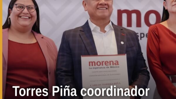 Carlos Torres Piña michoacán hablando ante militantes en un acto oficial en Michoacán, con bandera de México y logo de