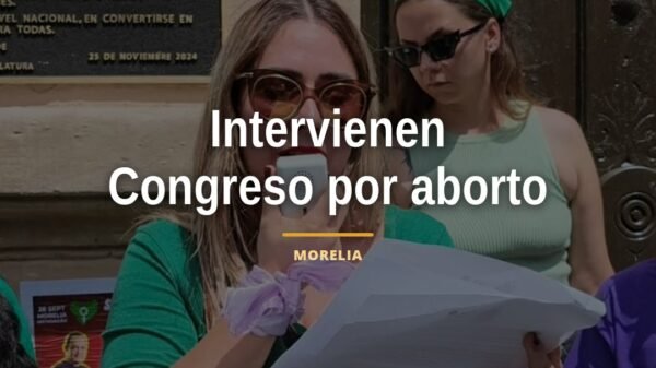 Mujeres colocan carteles con engrudo en la fachada del Congreso de Michoacán en Morelia, denunciando obstáculos al acceso al