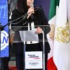 Tere Herrera hablando ante micrófonos y bandera de Michoacán durante su segundo informe legislativo en el Congreso del