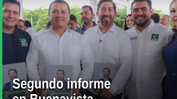 Abraham Espinoza Villa hablando ante público en evento del segundo informe en Buenavista, Michoacán, con logo del PVEM