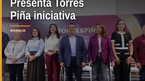 Carlos Torres Piña hablando frente a un micrófono con bandera de Morena, presentando 'La 4T te escucha' en Morelia