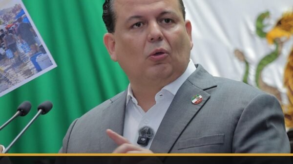 Fotografía de Memo Valencia hablando ante micrófonos en Morelia, con cartel de 'reforma código urbano' visible en fondo
