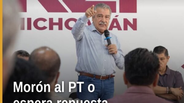Raúl Morón Orozco hablando ante micrófono en evento político en Morelia, con logo del Partido del Trabajo visible en fondo