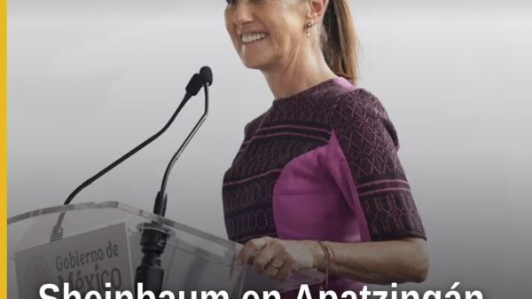 Claudia Sheinbaum hablando ante una multitud en Apatzingán, Michoacán, con banderas mexicanas al fondo, destacando la