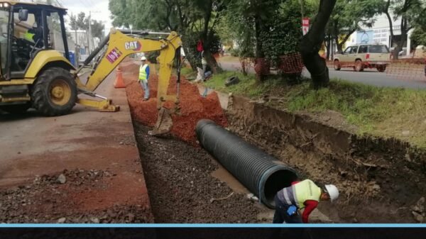 Obreros instalando tubería pluvial de gran diámetro en una calle del poniente de Morelia, con equipo pesado y señalización
